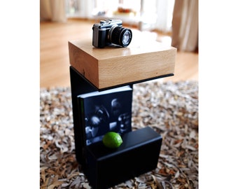 May include: A black metal side table with a wooden top. The table has a shelf underneath the top. A camera and a lime are on the top of the table.
