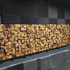 Puede incluir: Una pared cubierta con paneles de espuma ac&uacute;stica negra con un gran panel de madera dorada hecho de cuadrados peque&ntilde;os.