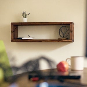 May include: A wooden shelf with a small potted plant, a book, and a metal deer figurine. The shelf is mounted on a white wall.