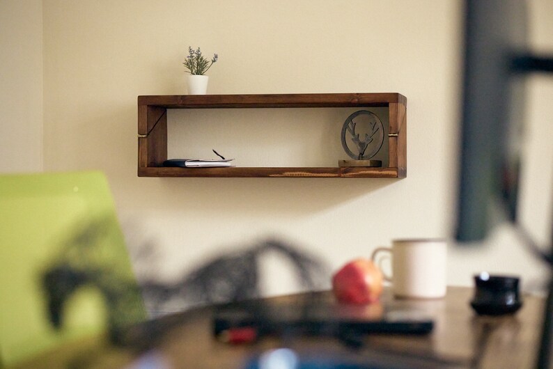 May include: A wooden shelf with a small potted plant, a book, and a metal deer figurine. The shelf is mounted on a white wall.