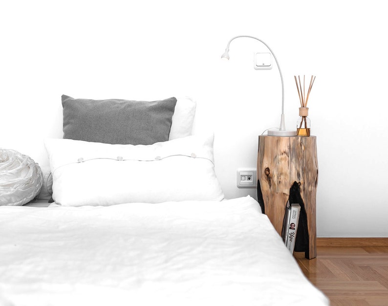 May include: A white bed with a gray pillow and a white pillow with buttons. A wooden nightstand with a lamp and a diffuser is next to the bed.