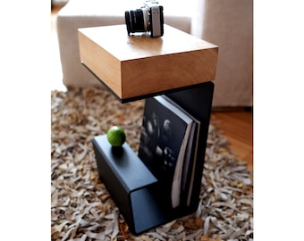 May include: A black metal side table with a wooden top. The table has a shelf for storing books or magazines. A camera and a green apple are on the top shelf.
