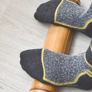 May include: A person's feet wearing black socks with yellow accents are rolling a wooden foot roller on a light wood floor.