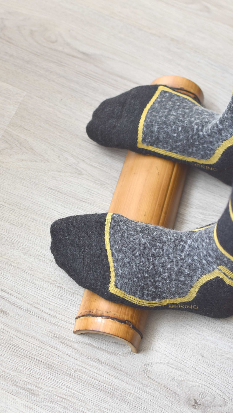 May include: A person's feet wearing black socks with yellow accents are rolling a wooden foot roller on a light wood floor.