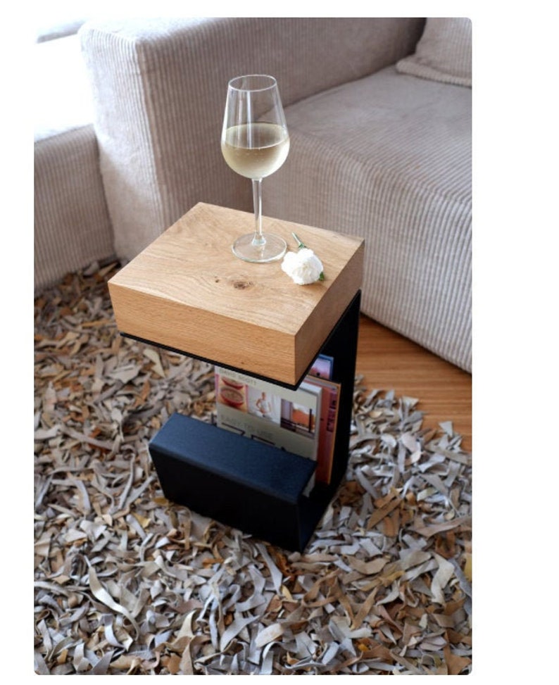 Puede incluir: Una peque&ntilde;a mesa auxiliar de madera con un marco de metal negro y un estante para libros. La mesa est&aacute; sobre una alfombra hecha de cuero desmenuzado. Un vaso de vino blanco se encuentra sobre la superficie de la mesa.