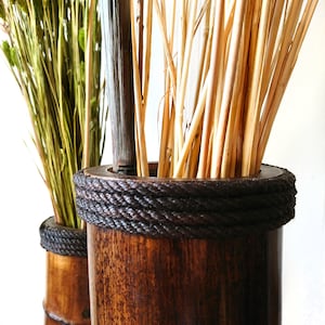 Puede incluir: Dos jarrones de bamb&uacute; marr&oacute;n con un ribete de cuerda marr&oacute;n oscuro. Los jarrones est&aacute;n llenos de ramitas secas de color marr&oacute;n claro.
