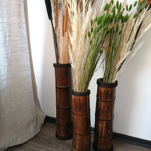 May include: Three tall brown bamboo vases with dried flowers and grasses. The vases are made of natural bamboo and have a rustic look. The flowers include wheat, cattails, and green grasses.