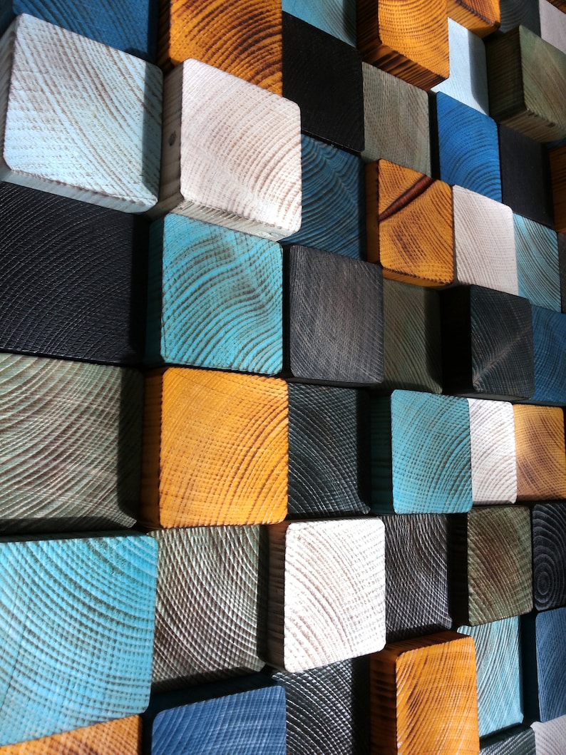 Puede incluir: Una pieza de arte de pared hecha de bloques de madera en varios colores, incluyendo azul, verde, negro, blanco y naranja. Los bloques est&aacute;n dispuestos en un patr&oacute;n geom&eacute;trico.