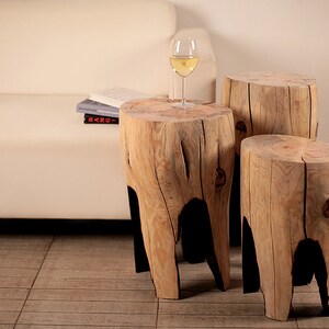 May include: Three wooden stump side tables with natural wood grain and black painted legs. The tables are arranged in a staggered formation with a glass of white wine on the middle table.