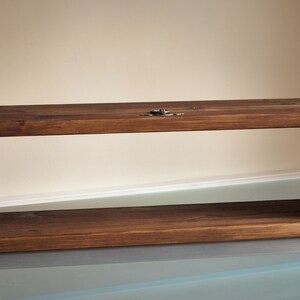 May include: A dark brown wooden shelf with a rectangular open frame. The shelf has a simple design with visible wood grain and is mounted to a wall.