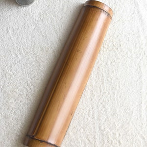 May include: A long, cylindrical, brown bamboo container with a smooth, polished surface. The container is lying on a white, fluffy surface.