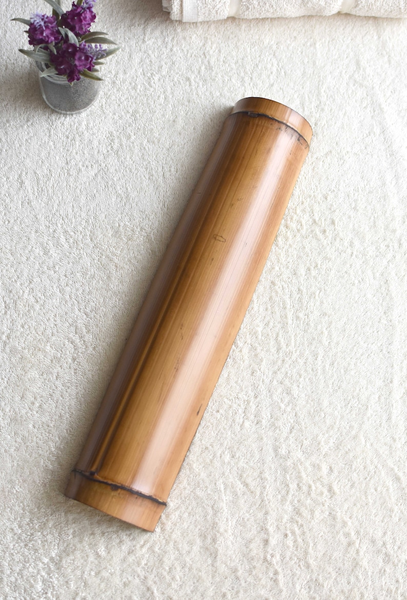May include: A long, cylindrical, brown bamboo container with a smooth, polished surface. The container is lying on a white, fluffy surface.