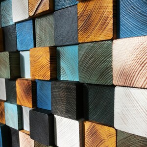 Puede incluir: Una pieza de arte de pared hecha de bloques de madera en varios tonos de azul, verde, marr&oacute;n y blanco. Los bloques est&aacute;n dispuestos en un patr&oacute;n escalonado, creando una superficie visualmente interesante y texturizada.