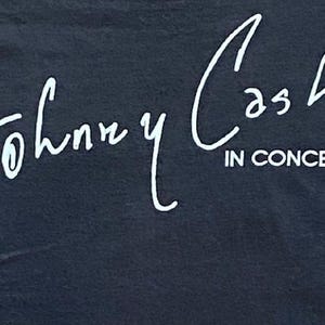 K&ouml;nnte beinhalten: Schwarzes T-Shirt mit dem wei&szlig;en Schriftzug "Johnny Cash IN CONCERT" in kursiver Schrift. Der Text sieht aus wie eine Unterschrift. Das T-Shirt besteht aus einem dunklen Stoff.