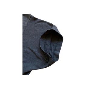 K&ouml;nnte beinhalten: Nahaufnahme eines dunkelgrauen V-Ausschnitt-T-Shirts. Das Bild konzentriert sich auf den &Auml;rmel- und Schulterbereich und zeigt die Stoffstruktur und die Nahtdetails. Das Shirt scheint aus einem weichen, bequemen Material zu sein.
