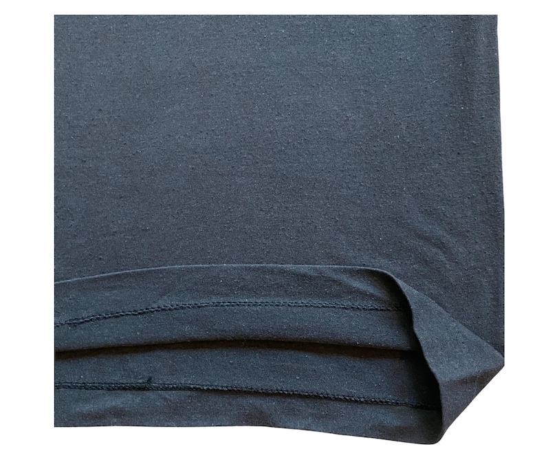 K&ouml;nnte beinhalten: Nahaufnahme eines dunkelmarineblauen Stoffes, m&ouml;glicherweise ein T-Shirt oder ein anderes Kleidungsst&uuml;ck. Der Stoff hat ein leicht strukturiertes Aussehen. Der Saum ist sichtbar, mit einer gefalteten Kante und einer Doppelnaht.