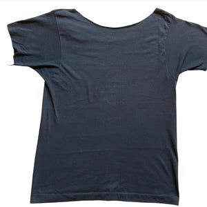 K&ouml;nnte beinhalten: Ein dunkelmarineblaues T-Shirt mit weitem Rundhalsausschnitt. Die kurzen &Auml;rmel sind sichtbar, und das Shirt besteht aus einem weichen, wahrscheinlich Baumwollmaterial. Das Shirt ist vor einem wei&szlig;en Hintergrund fotografiert.
