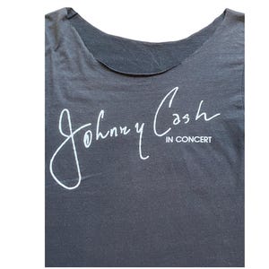 K&ouml;nnte beinhalten: Dunkelgraues T-Shirt mit der wei&szlig;en Unterschrift von Johnny Cash und dem Text "IN CONCERT" darunter. Das Oberteil hat einen Rundhalsausschnitt und ist aus weichem Stoff gefertigt.