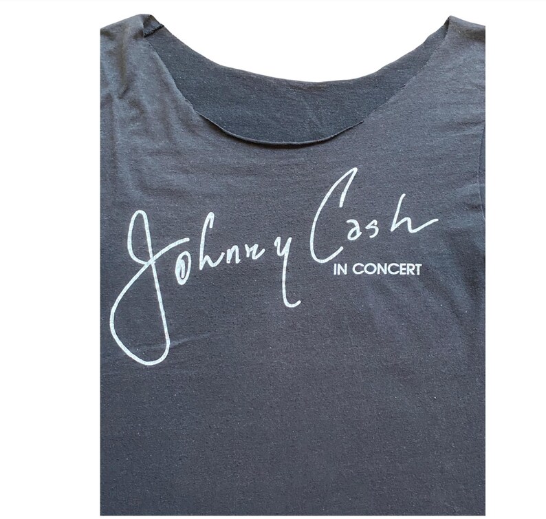 K&ouml;nnte beinhalten: Dunkelgraues T-Shirt mit der wei&szlig;en Unterschrift von Johnny Cash und dem Text "IN CONCERT" darunter. Das Oberteil hat einen Rundhalsausschnitt und ist aus weichem Stoff gefertigt.