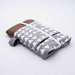 May include: A grey and white fabric pouch with a brown leather flap and a white elastic strap. The pouch has a white triangle pattern and the text "elotte" is visible on the flap.