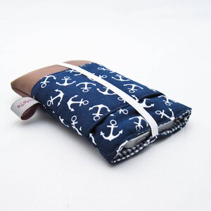 May include: A blue and white fabric phone case with a white anchor pattern. The case has a brown flap and a white elastic strap.