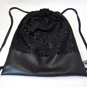 Peut inclure: Un sac à cordon noir avec un dessus pailleté et un fond en cuir noir. Le sac a un long cordon.