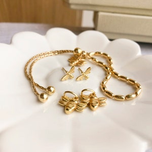 May include: A set of gold bee jewelry, including a bracelet, earrings, and charms. The bracelet is a chain with gold beads, and the earrings and charms are shaped like bees.