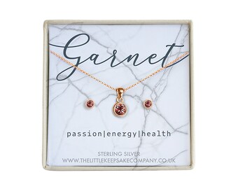 Könnte beinhalten: Ein Granat-Halsketten- und Ohrring-Set in einer weißen Schachtel mit Marmormuster. Die Schachtel trägt die Aufschrift "Garnet", "passion|energy|health", "Sterling Silver" und "www.thelittlekeepsakecompany.co.uk".