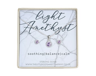 Könnte beinhalten: Eine kleine Geschenkbox mit einer silbernen Halskette und Ohrringen mit einem hellblauen Amethyststein. Die Box hat ein marmorartiges Muster und den Text "light amethyst soothing|balance|calm STERLING SILVER www.thelittlekeepsakecompany.co.uk" aufgedruckt.