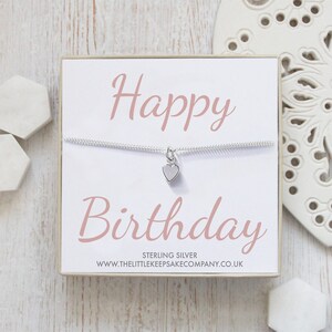 Op de afbeelding: Een witte kaart met de woorden "Happy Birthday" in roze schrift. Een zilveren ketting met een klein hartje als hanger wordt op de kaart getoond. De kaart zit in een witte doos met de tekst "Sterling Silver" en een websiteadres.