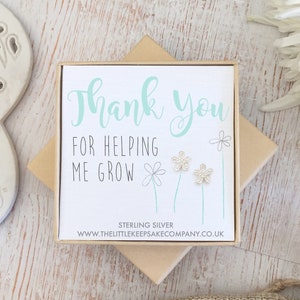 Op de afbeelding: Een klein cadeaudoosje met een witte kaart waarop staat: "Bedankt voor je hulp bij het groeien." De kaart heeft een zilveren bloemenontwerp en de woorden "Sterling Silver" en "www.thelittlekeepsakecompany.co.uk" staan ​​onderaan gedrukt.