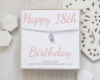 May include: A white gift box with a silver necklace inside. The necklace has a small heart charm. The box has the text "Happy 18th Birthday" in pink lettering. The text "Sterling Silver" and "www.thelittlekeepsakecompany.co.uk" is printed on the bottom of the box.