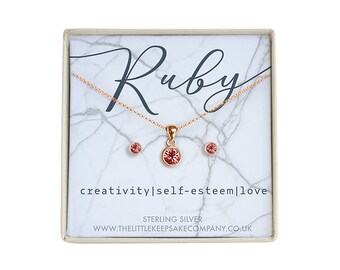 Könnte beinhalten: Ein rosafarbenes Rubin-Halsketten- und Ohrring-Set in einer weißen Schachtel mit den Worten "Ruby", "creativity|self-esteem|love" und "STERLING SILVER" darauf gedruckt. Die Schachtel enthält auch die Website-Adresse "www.thelittlekeepsakecompany.co.uk".