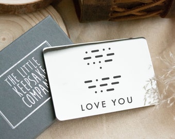 Könnte beinhalten: Eine silberne Metallkarte mit den Worten "LOVE YOU" eingraviert. Die Karte enthält auch zwei Reihen von Braille-Punkten.