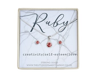 Könnte beinhalten: Ein silbernes Halsketten- und Ohrring-Set mit einem roten Edelstein-Anhänger und Ohrringen. Die Schachtel trägt den Namen "Ruby" und die Worte "creativity|self-esteem|love" sind darauf gedruckt. Die Schachtel trägt außerdem die Aufschrift "Sterling Silver" und "www.thelittlekeepsakecompany.co.uk".