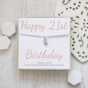 Op de afbeelding: Een witte cadeaudoos met een zilveren ketting erin. De ketting heeft een klein zilveren hartje als hanger. De doos heeft de tekst "Happy 21st Birthday" in roze letters en de tekst "Sterling Silver www.thelittlekeepsakecompany.co.uk" in zwarte letters.