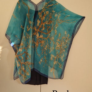 May include: A turquoise blue sheer shawl with a printed design of a tree with white blossoms. The shawl is draped over a hanger and has a V-neckline. The back of the shawl is shown in the image. The text "Back" is printed below the shawl.