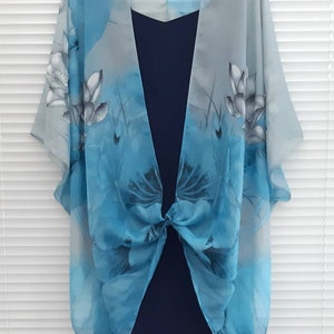 May include: A sheer blue and gray floral print kimono with a knotted front. The kimono is draped over a navy blue dress.