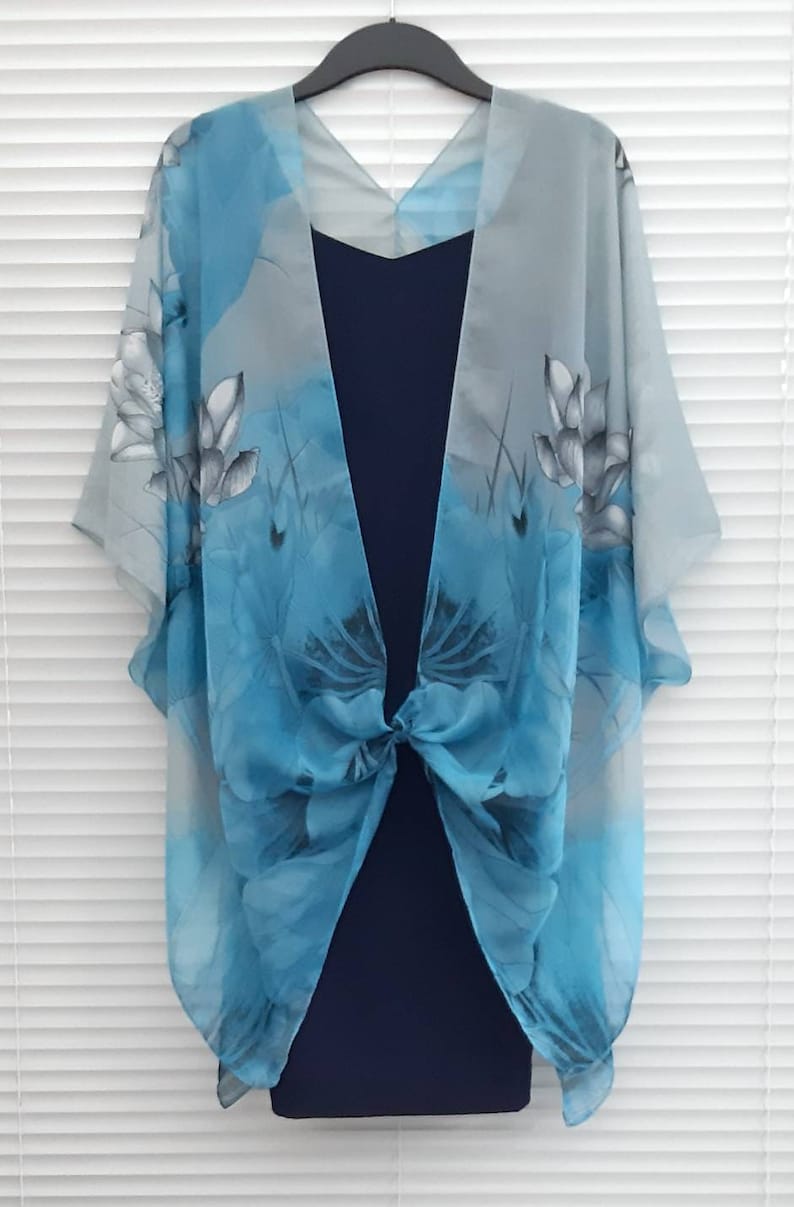 May include: A sheer blue and gray floral print kimono with a knotted front. The kimono is draped over a navy blue dress.
