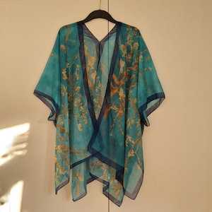 May include: A turquoise blue sheer kimono with a floral print and a dark blue trim. The kimono is made of a lightweight fabric and has a relaxed fit.