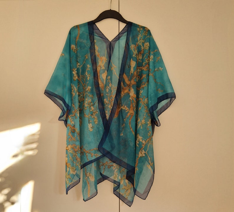 May include: A turquoise blue sheer kimono with a floral print and a dark blue trim. The kimono is made of a lightweight fabric and has a relaxed fit.