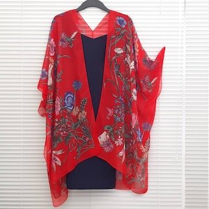 May include: Red sheer kimono with a floral print featuring hummingbirds and flowers. The kimono is open at the front and has a V-neck.