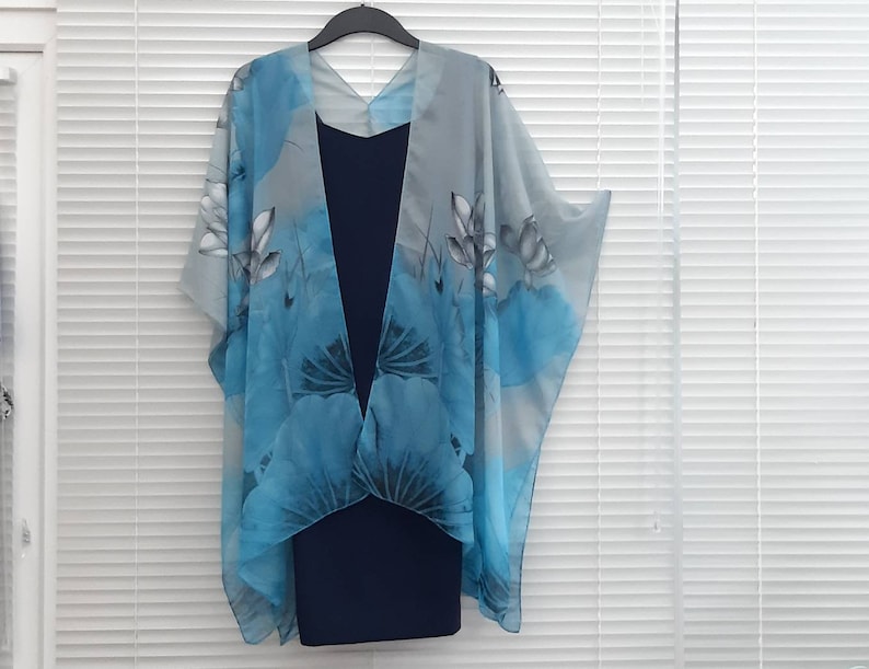 May include: A light blue sheer kimono with a floral print. The kimono has a V-neck and is made of a lightweight fabric. It is paired with a dark blue dress.