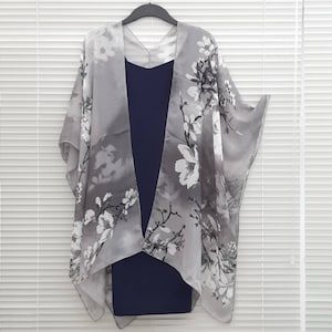May include: A grey sheer kimono with a white floral print. The kimono is draped over a navy blue dress.