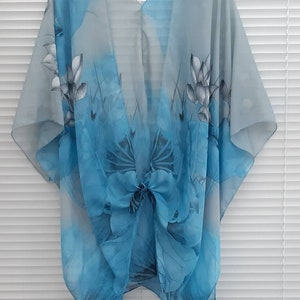 May include: A light blue sheer kimono with a floral print. The kimono has a V-neck and a tie at the waist.