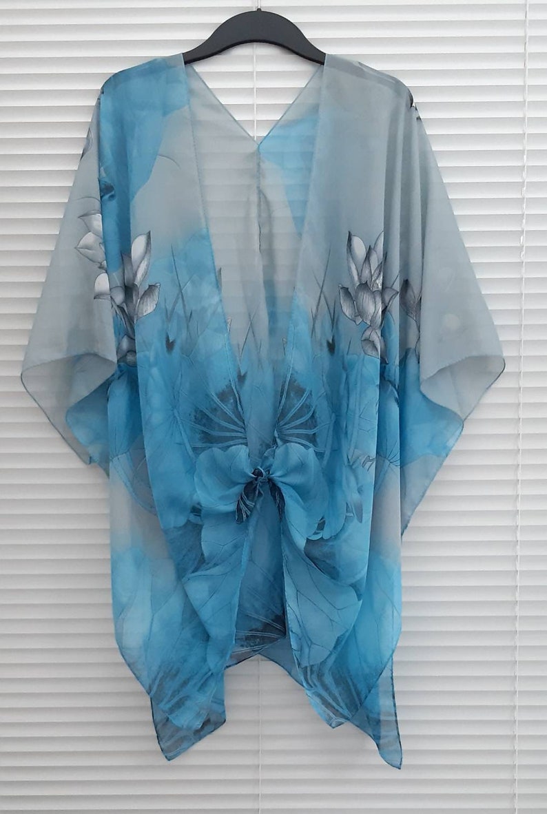 May include: A light blue sheer kimono with a floral print. The kimono has a V-neck and a tie at the waist.