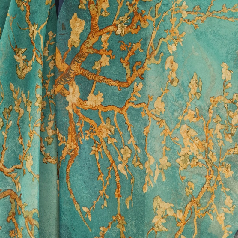May include: A teal blue silk scarf with a printed design of a stylized tree with yellow blossoms. The scarf is a soft, flowing fabric with a delicate feel.