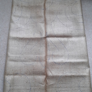Peut inclure: Un morceau de tissu rectangulaire beige clair avec une texture tissée visible. La surface présente un motif répétitif de lignes pointillées bleu foncé formant des formes incurvées en goutte d'eau réparties sur tout le matériau.