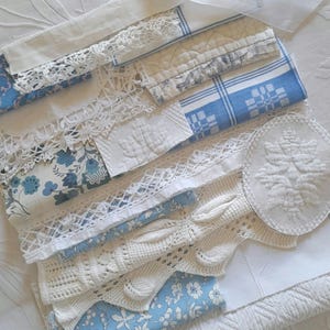 May include: An assortment of vintage textiles in white and blue hues. The collection features lace, floral prints, and embroidered details. Various patterns and textures are visible, including crochet and quilted fabrics. The arrangement suggests a focus on antique or handmade items.