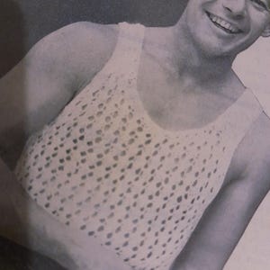 May include: A white, open-weave crochet tank top. The top features a scoop neck and wide straps. The crochet pattern creates a textured, airy design. The garment is likely handmade.